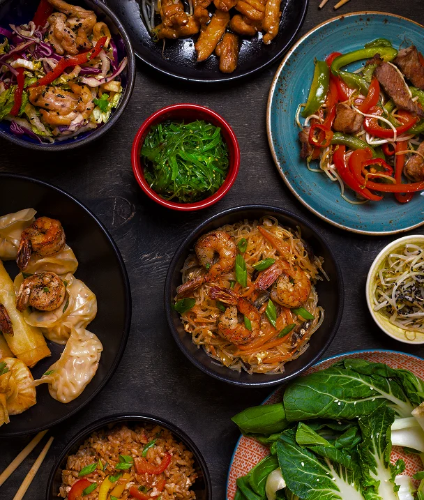 Een overzicht van diverse Aziatische gerechten, waaronder noedels, garnalen, dumplings, groenten, rijst en geglazuurd vlees.