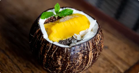Vers mangodessert geserveerd in een kokosschaal met chiazaad, kokosvlokken en munt.