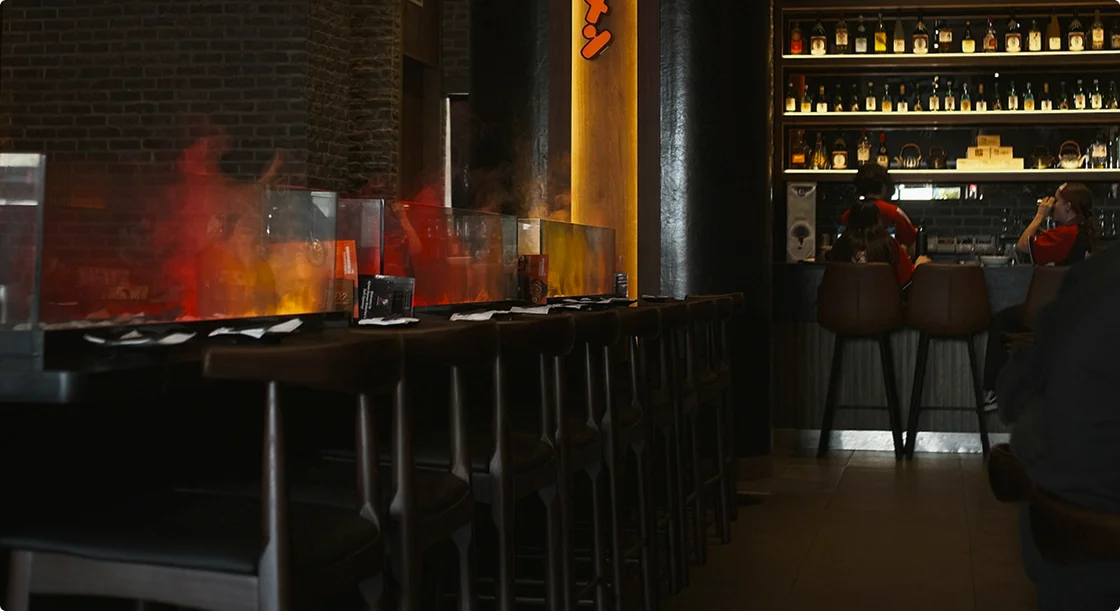 Een donkere en sfeervolle Aziatische restaurantinterieur met zitplaatsen aan de bar, warme verlichting en een stijlvolle bar.