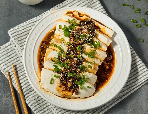 Zijdezachte tofu geserveerd met een hartige pittige saus, sesamzaad en versgehakte bosuitjes.